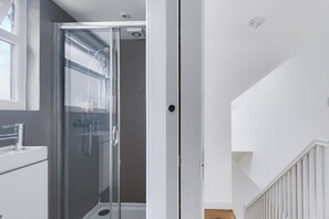 Ein modernes Badezimmer mit einer Duschkabine, einem weißen Waschbecken und einem Fenster.