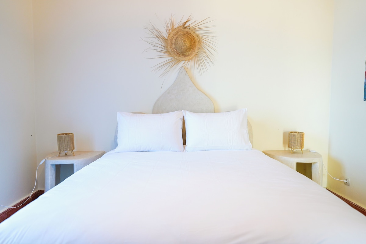 A bed with white linens, two bedside tables with lamps, and a wall-mounted decorative piece.