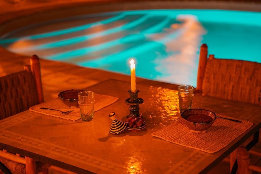 Mesa con vela, vasos y un tazón, frente a una piscina con tonalidades azules.