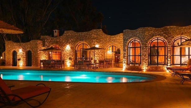 A swimming pool with stone walls and arched windows, surrounded by outdoor seating.