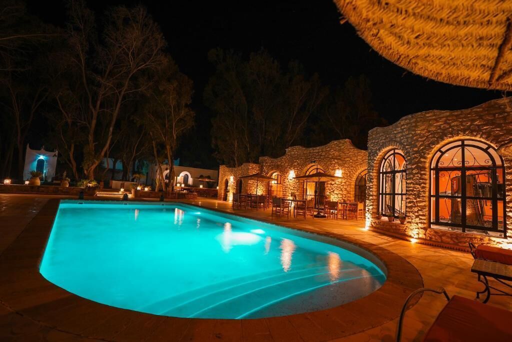 Ein beleuchteter Pool bei Gebäuden aus Stein und mit Sitzgelegenheiten im Freien.