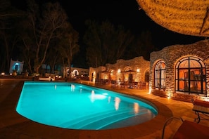 A nighttime swimming pool with stone buildings and outdoor seating.