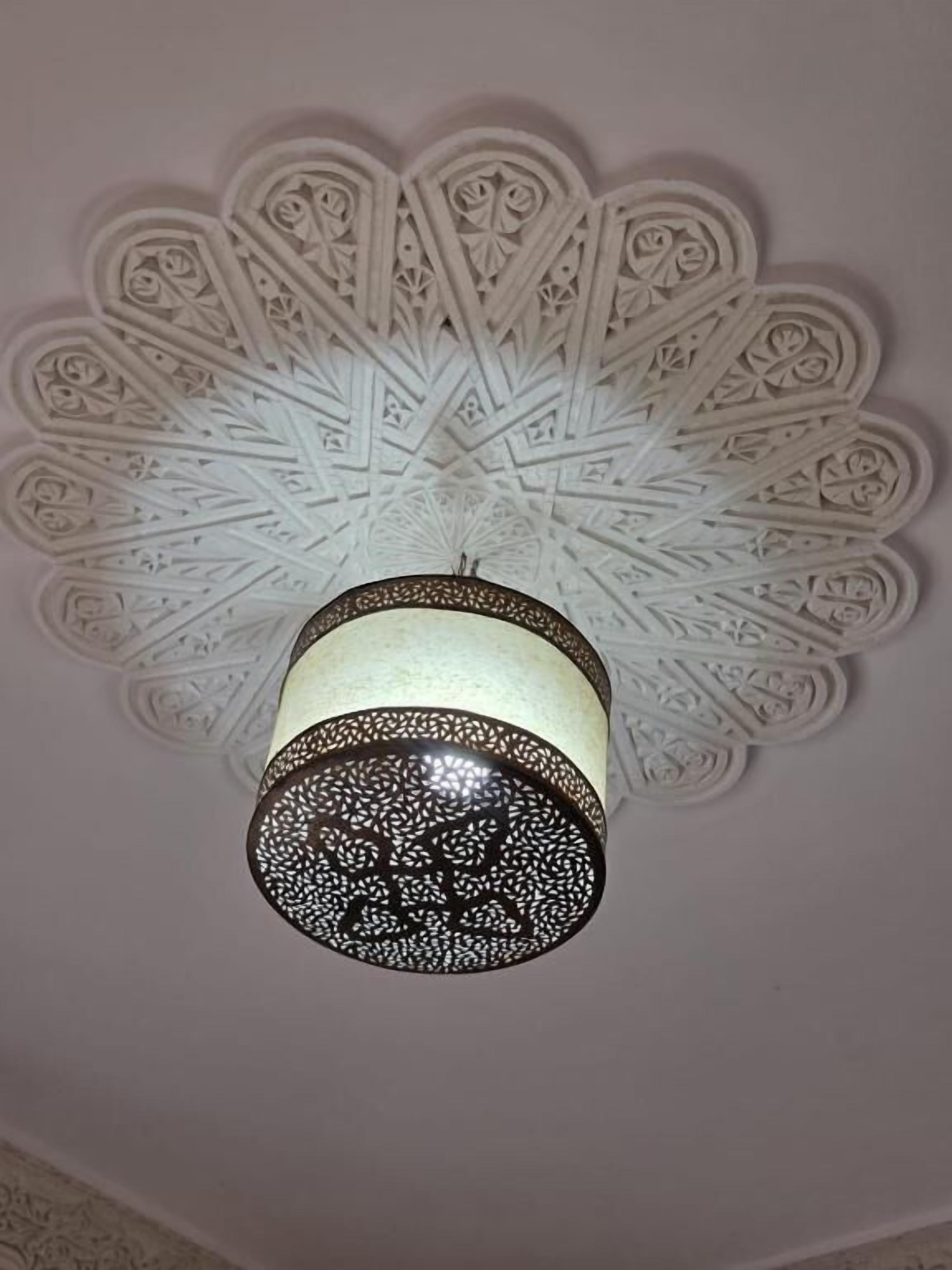 Un plafond orné de motifs blancs complexes et un luminaire suspendu.