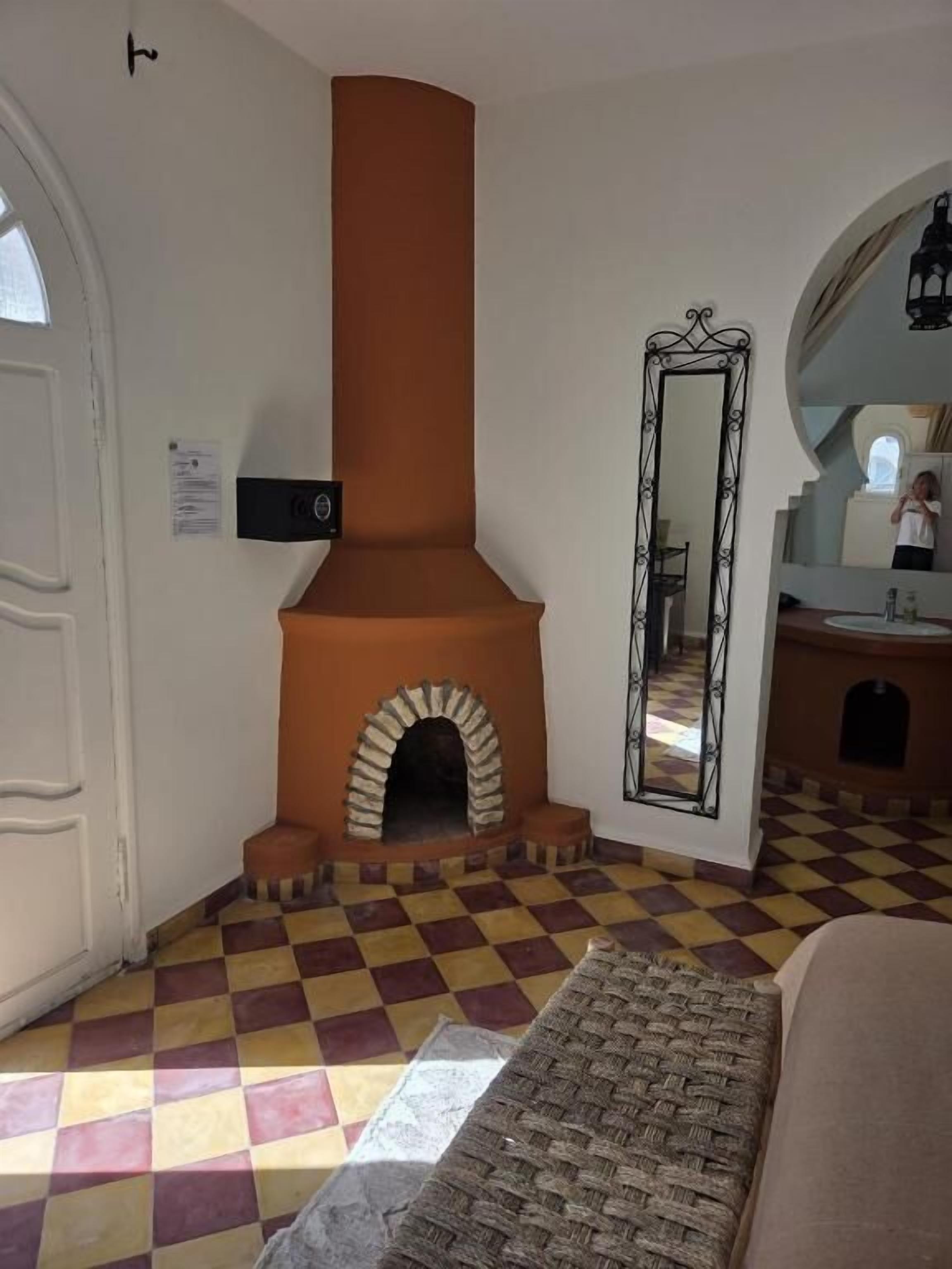 Una habitación con piso de cuadros, chimenea, espejo y puerta.