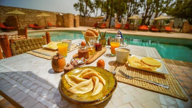 A breakfast table with a bowl of food, a plate of pancakes, and various beverages near a poolside setting.