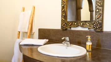 Uma casa de banho com uma pia redonda, um espelho com moldura ornamentada e um porta-toalhas.