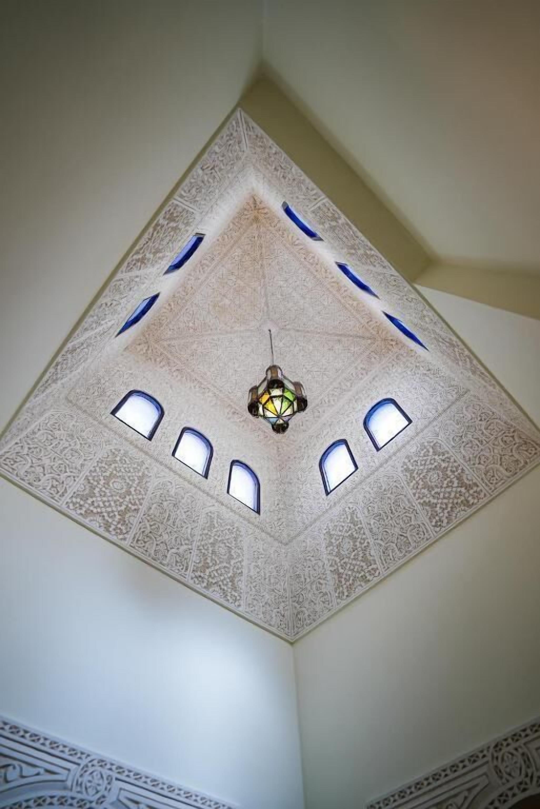 Een plafond met ingewikkelde geometrische patronen en een centraal lichtarmatuur.
