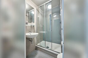 Ein modernes Badezimmer mit einer gläsernen Duschkabine, einem Waschbecken und einem Spiegel.