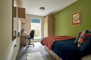 Ein Schlafzimmer mit Bett, Schreibtisch, Stuhl und Fenster.