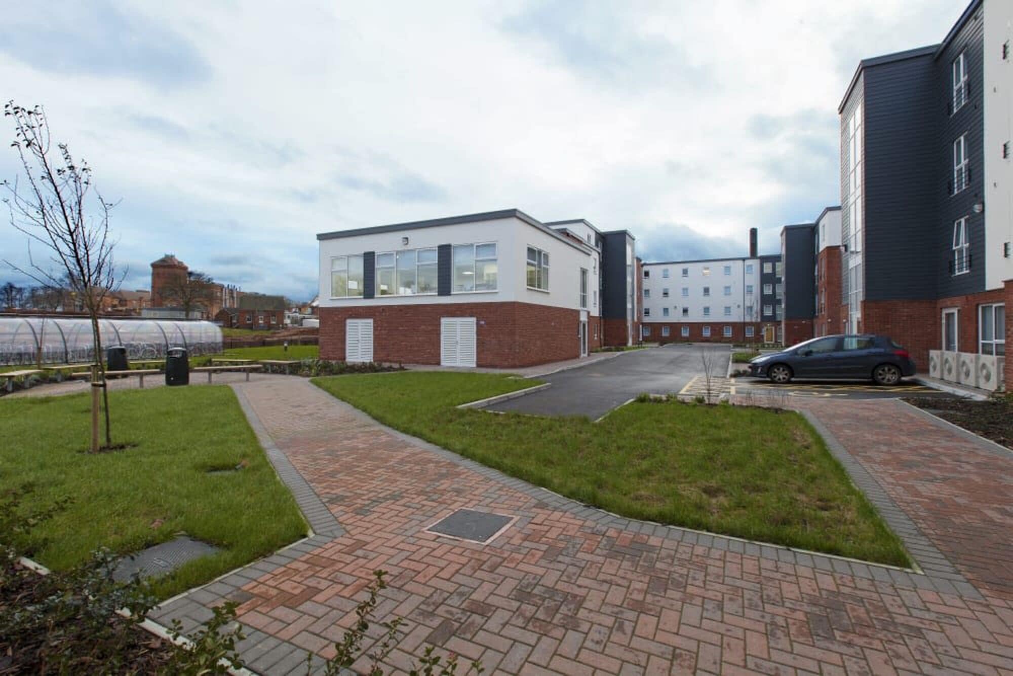 A modern building with a brick facade, a paved walkway, and a car parked nearby.