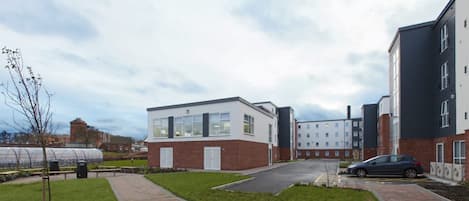 A modern building with a brick facade, a paved walkway, and a car parked nearby.