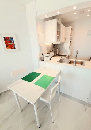 A modern kitchen with white cabinets, a stainless steel sink, and a dining area with a white table and chairs. - Modern studio apartment right on the beach promenade (Torrox-Costa)