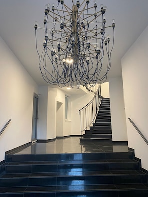 A staircase with a modern chandelier and black-tiled steps. - Cosy, peaceful loft double bed 1.50 meters above ground (soundproof). (Berlin)