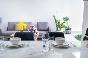 Ein Essbereich mit einem Marmortisch, gedeckt für vier Personen, einer Couch im Hintergrund und Topfpflanzen.