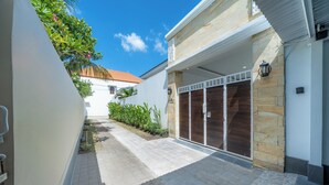 A modern building with a stone facade, a gated entrance, and a paved walkway. - Addikha Villa by Betterplace (Canggu)