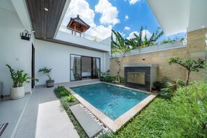 Zona de piscina exterior moderna amb una llar de pedra, plantes en testos i un cel blau clar.