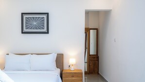 A hotel room with a bed, a nightstand with a lamp, a wooden wardrobe, and a framed artwork on the wall. - Addikha Villa by Betterplace (Canggu)