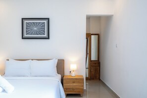 A hotel room with a bed, a nightstand with a lamp, a wooden wardrobe, and a framed artwork on the wall. - Addikha Villa by Betterplace (Canggu)