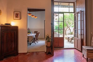 Un umbral abierto que da a un comedor con mesa y sillas, una planta en maceta y vistas al exterior.