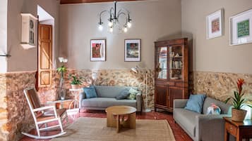 A cozy living room with a stone wall, a wooden cabinet, a grey sofa, a wooden coffee table, and a chandelier.