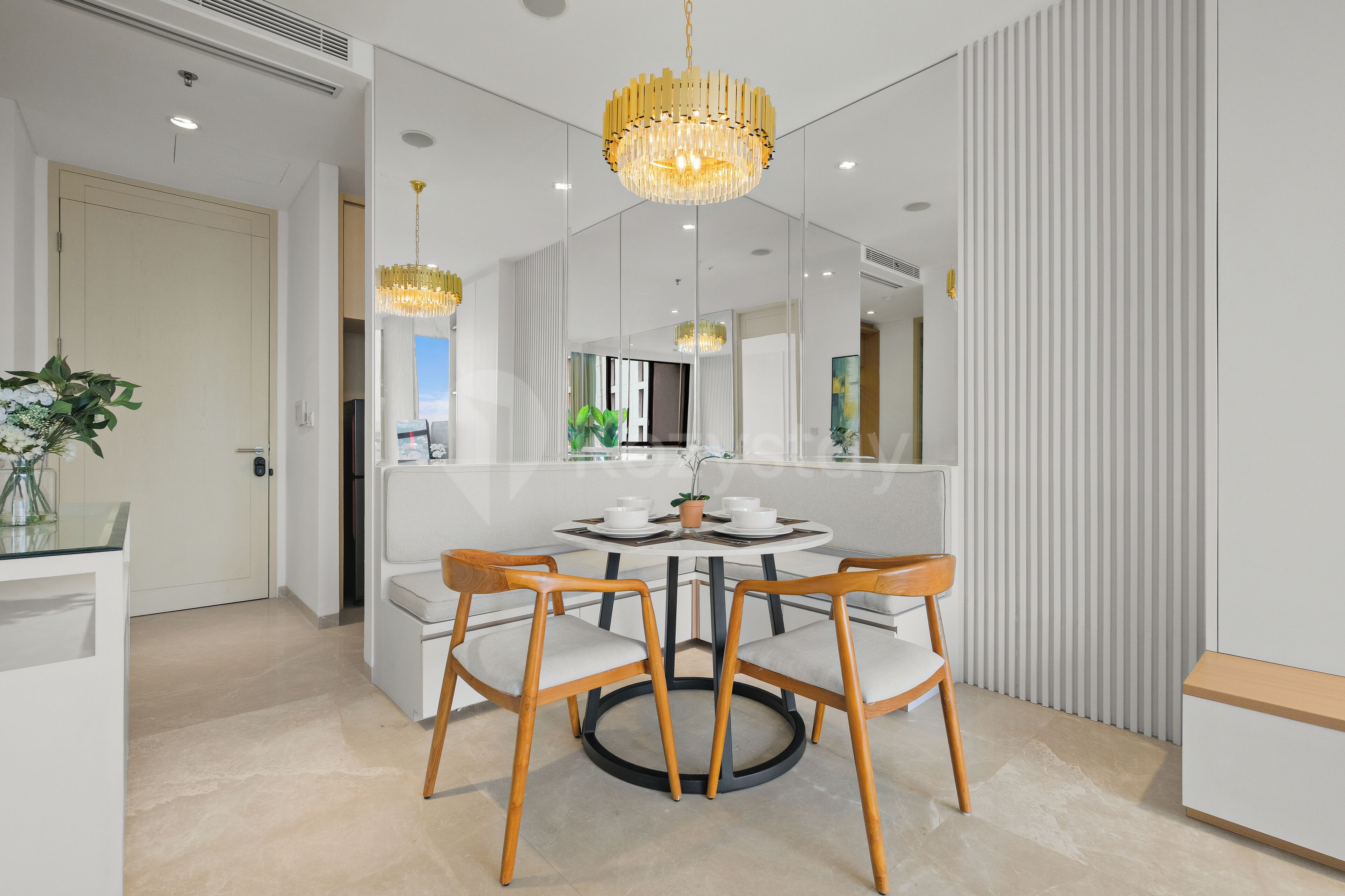 A modern dining area with a round table, four wooden chairs, and two chandeliers.