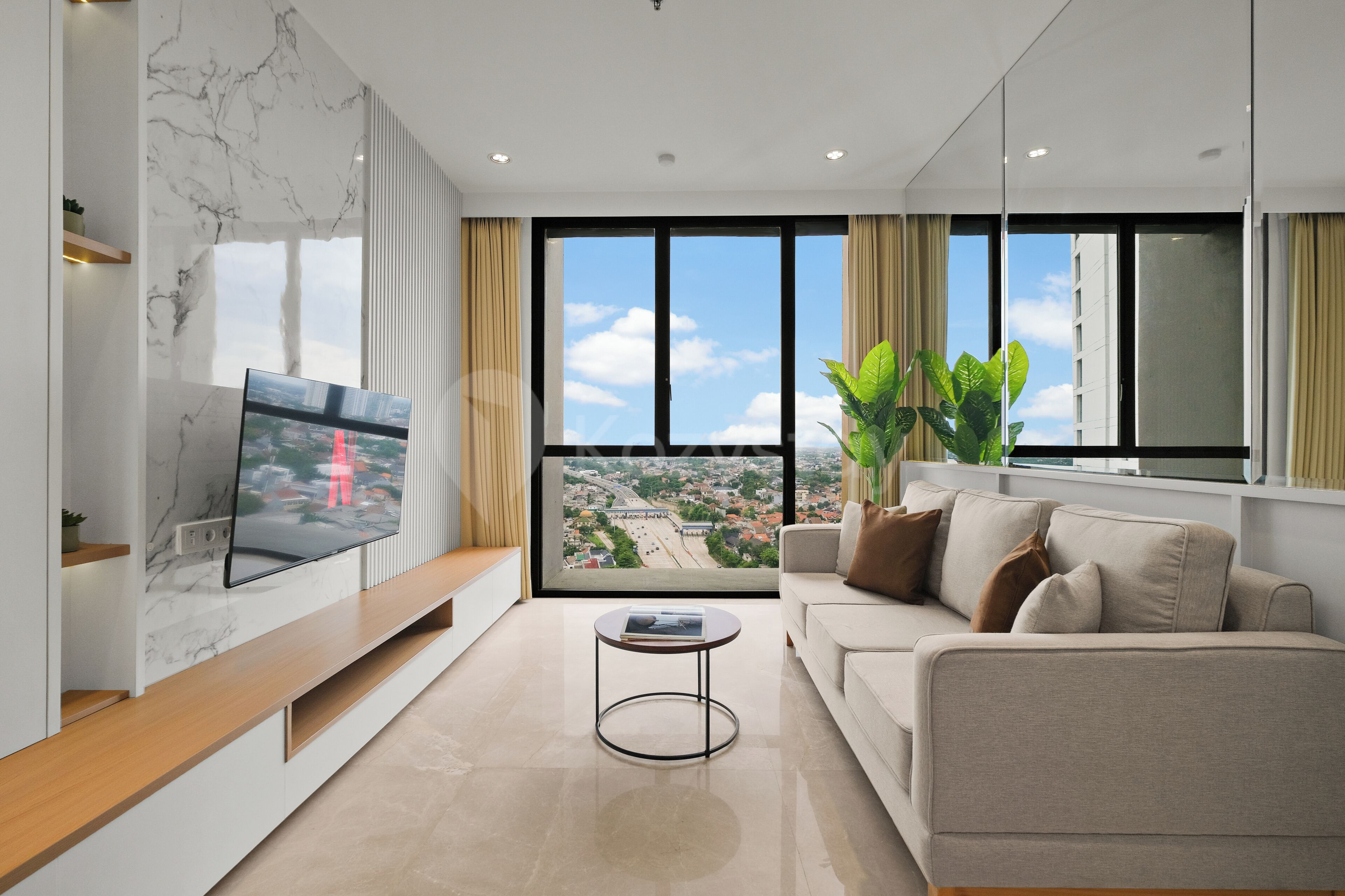 A modern living room with a flat-screen TV, a sofa, a coffee table, and a large window offering a city view.
