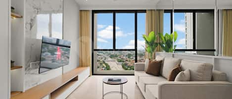 Una sala de estar moderna con un televisor de pantalla plana, un sofá, una mesa de centro y un ventanal con vistas a la ciudad.