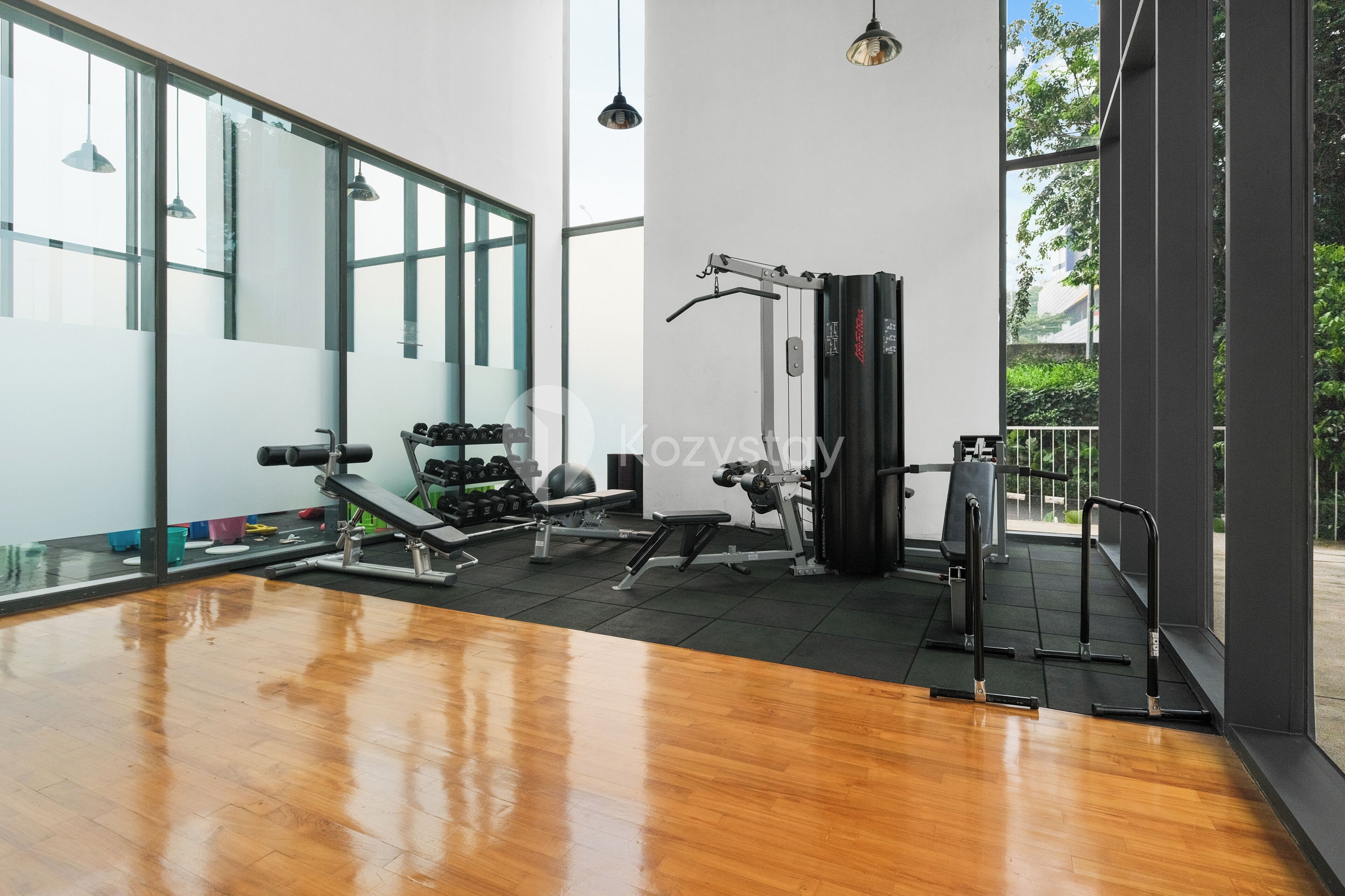 A gym with exercise equipment, large windows, and a wooden floor.