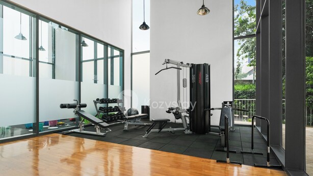 A gym with exercise equipment, large windows, and a wooden floor. - Brunn by Kozystay - Cilandak (South Jakarta)