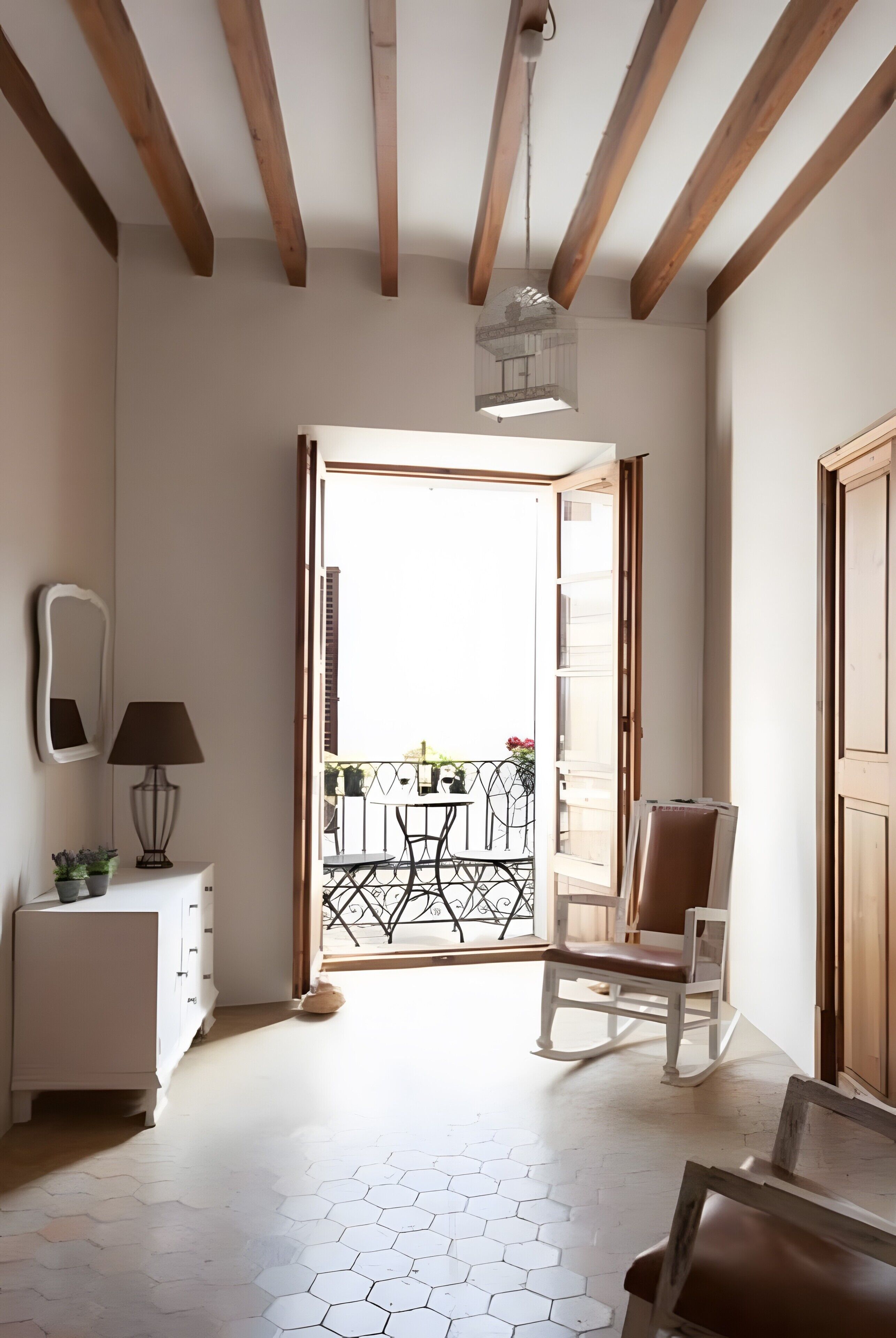Een kamer met een houten plafond, een witte vloer, een stoel, een tafel, een lamp en uitzicht op een buitenbalkon met een hekwerk.