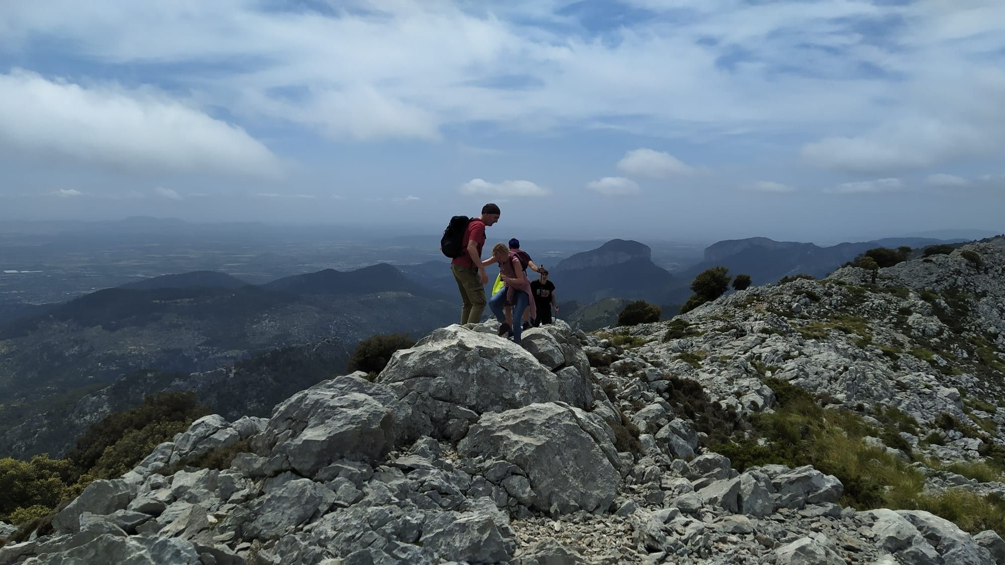 Un grupo de personas en la cima de una montaña rocosa con vistas a montañas y valles distantes.