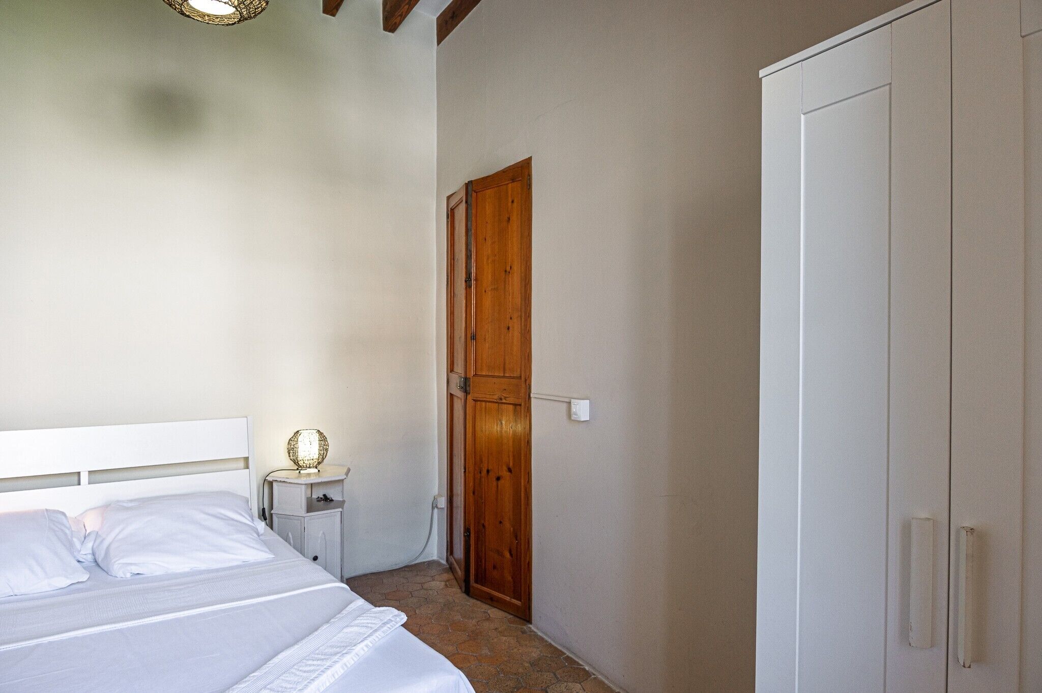 Een slaapkamer met een bed, nachtkastje, houten deur en een kledingkast.