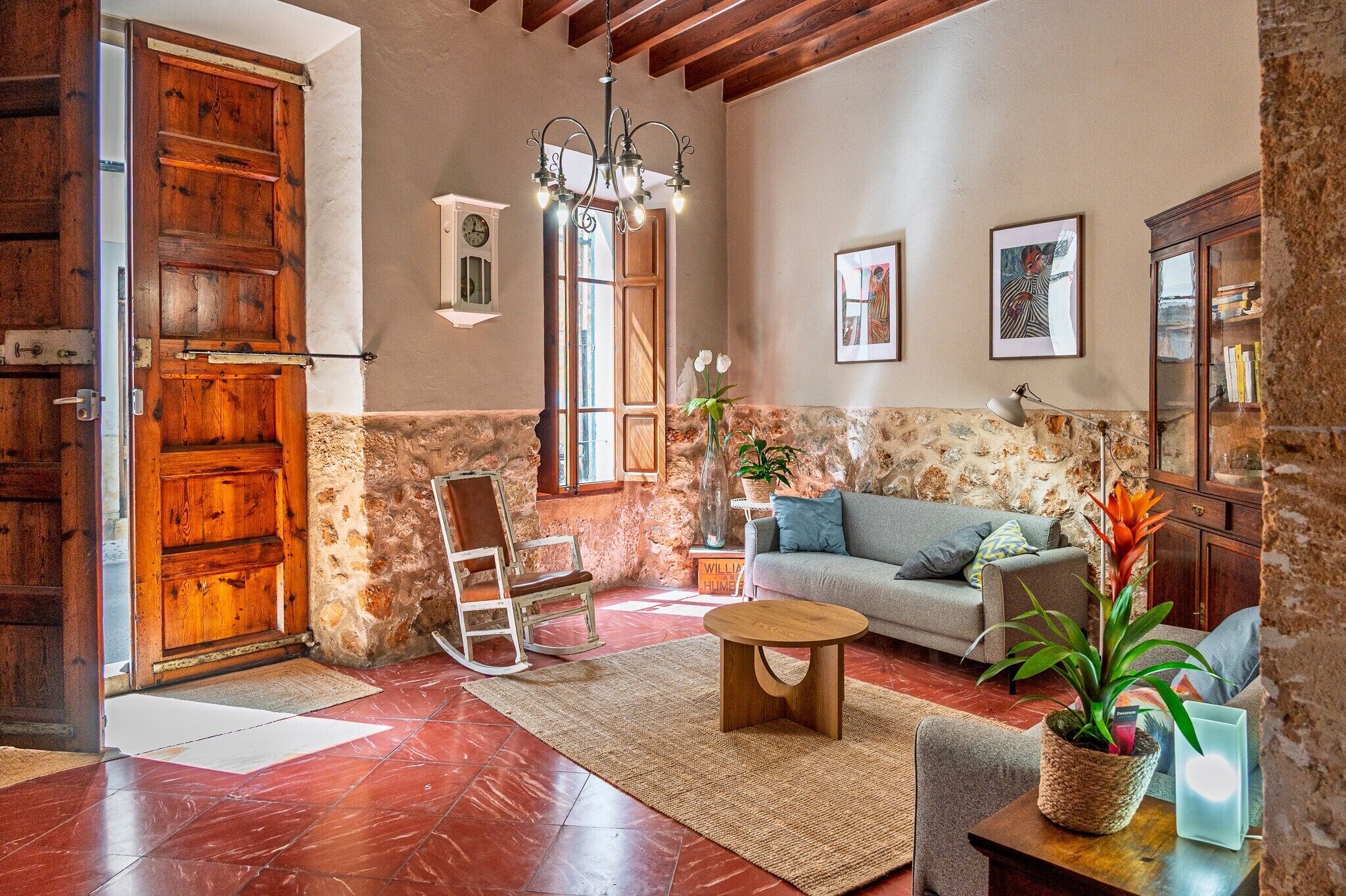 A rustic living room with a wooden door, a stone wall, a rocking chair, a sofa, and a chandelier.