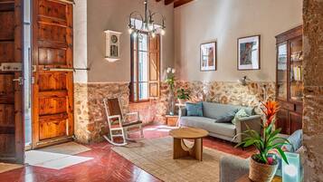 A rustic living room with a wooden door, a stone wall, a rocking chair, a sofa, and a chandelier.