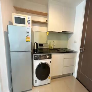 A compact kitchen with a built-in microwave, a washing machine, and a sink. - Cozy Private Home - Steps to BTS & MRT Sukhumvit (Krung Thep Maha Nakhon)