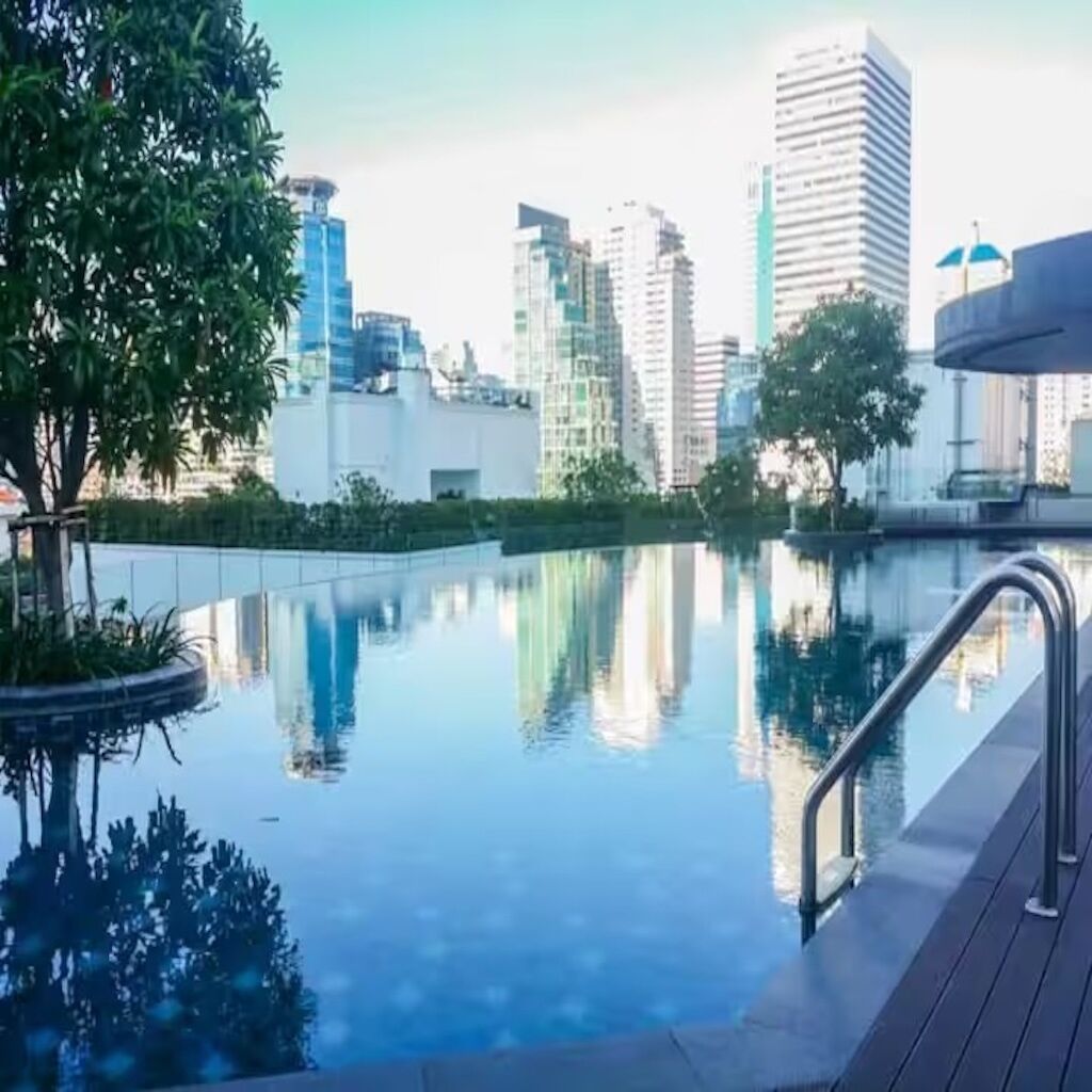 A swimming pool with a metal railing, surrounded by greenery and buildings in the background.
