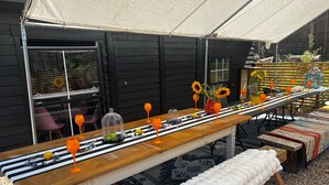 Una larga mesa de madera dispuesta con copas de vino naranja, girasoles y una variedad de frutas y verduras bajo una marquesina.