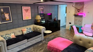 Una sala moderna con un sofá gris, una mesita redonda pequeña y un reposapiés rosa.