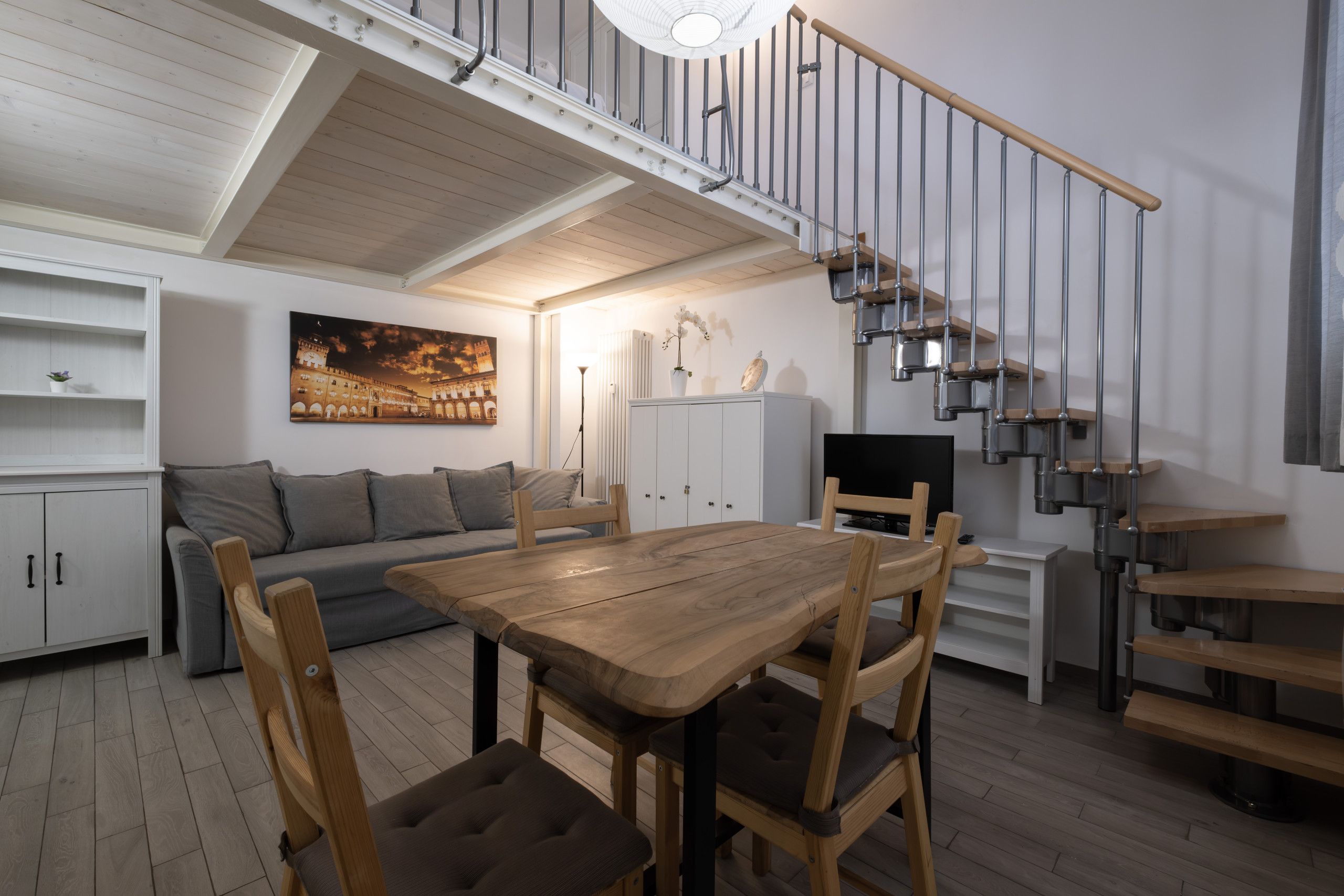A modern interior with a dining area, sofa, staircase, and artwork.