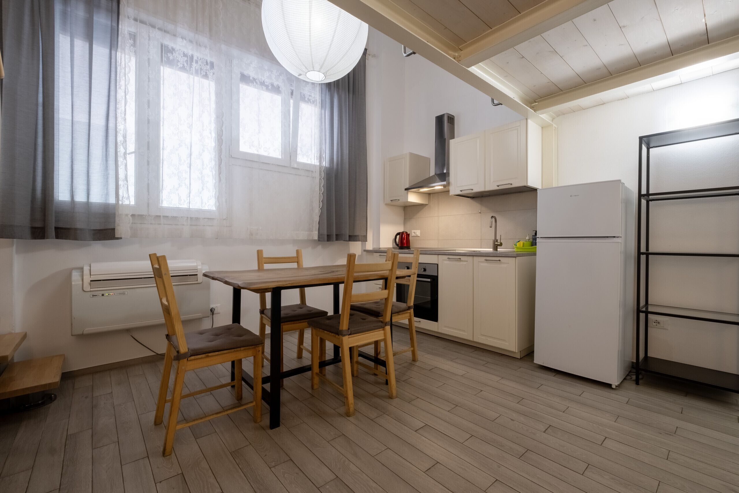 A kitchen with a dining table, chairs, a stove, a refrigerator, and a window with curtains.
