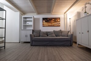 Un salón en tonos neutros, con un sofá gris, una estantería blanca y un cuadro con una vista urbana en la pared.