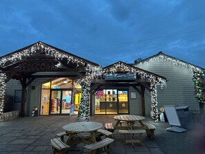 Ein Gebäude mit einem 'Welcome'-Schild, einem 'Cook's'-Schild und einem Weihnachtsbaum. Vor dem Gebäude befinden sich Picknicktische.