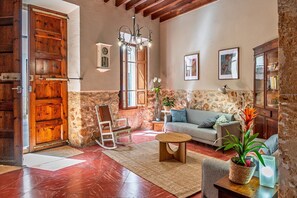 Una sala de estar rústica con puerta de madera, pared de piedra, una mecedora, un sofá y una araña.