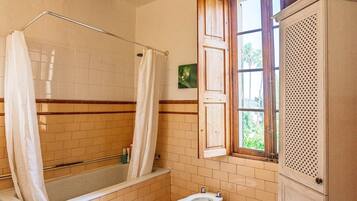 Een badkamer met een bad, douchegordijn, toilet en een raam met uitzicht op groen.
