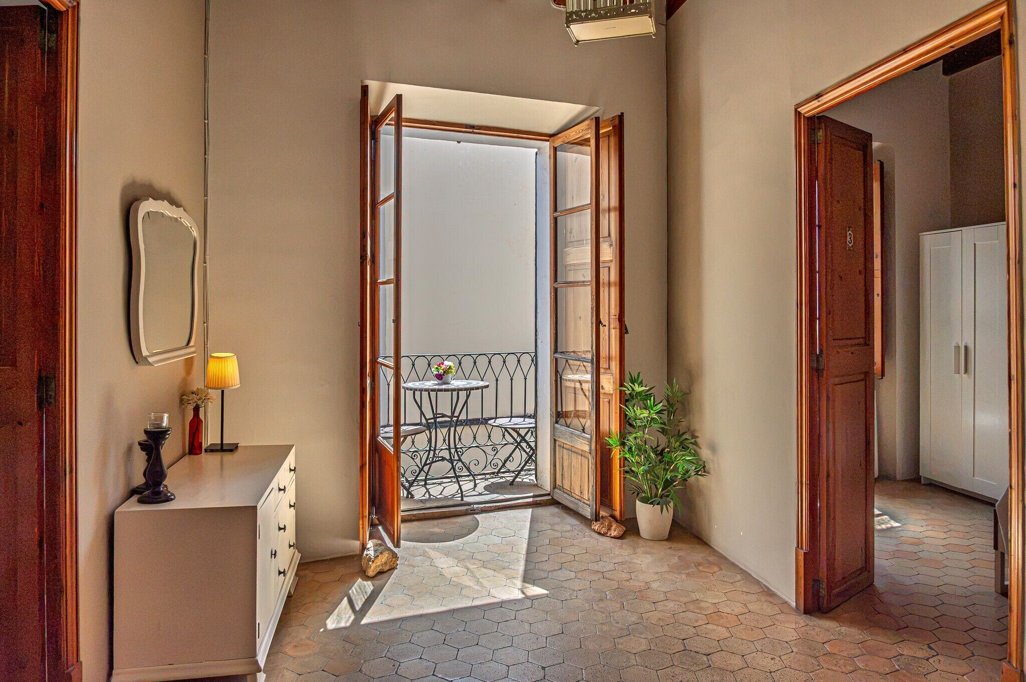 A hallway with a view to a balcony, a potted plant, and a dresser with a lamp.
