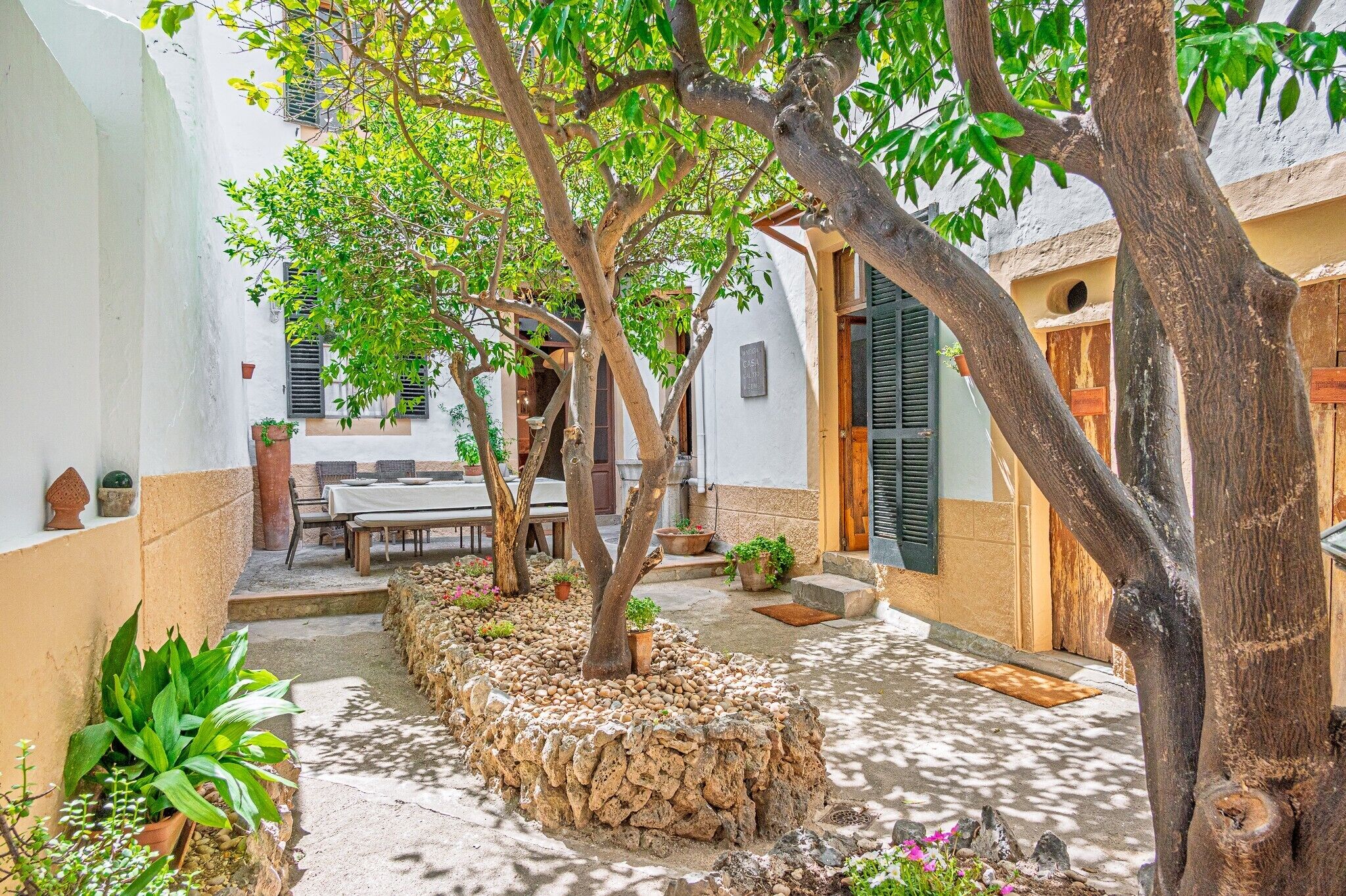 A courtyard with a dining table, chairs, potted plants, and a stone wall.