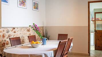 A dining area with a round table, chairs, a bowl of fruit, and a vase with flowers.