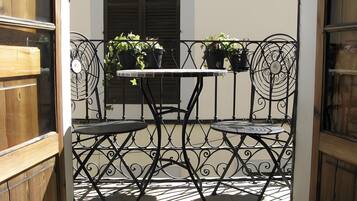 A small outdoor seating area with a table and two chairs, surrounded by a decorative metal fence, and potted plants on the fence.