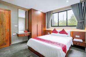 A hotel room with a bed, a wardrobe, a mirror, a window with curtains, and a bedside table.