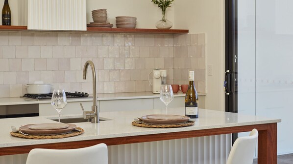 A modern kitchen with a central island, a stainless steel sink, and a wine bottle on the counter.